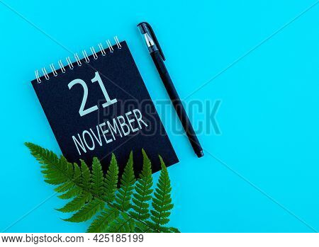 November 21th. Day 21 Of Month, Calendar Date. Black Notepad Sheet, Pen, Fern Twig, On A Blue Backgr