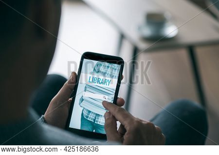 a young caucasian man, sitting at a coffee table in his living room, searches an ebook to lend on an online library with his smartphone, with a simulated search engine in its screen