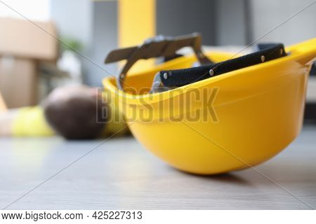Yellow Worker Helmet On Floor Beside Motionless Construction Worker
