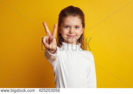 Attractive Girl Kid Showing Peace Gesture And Looking At Camera Isolated Against Bright Yellow Backg