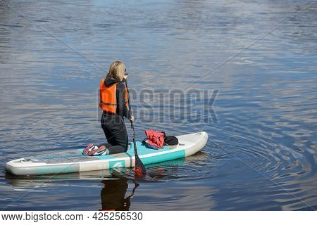 Vyborg, Russia, May 2, 2021-young Woman In Sports Outfit And Orange Life Vests Surfs On Supboard Kne