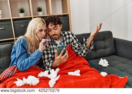 Young ill couple having medical teleconsultation using smartphone at home.