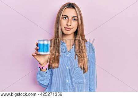 Beautiful hispanic woman holding earwax cotton removers thinking attitude and sober expression looking self confident 