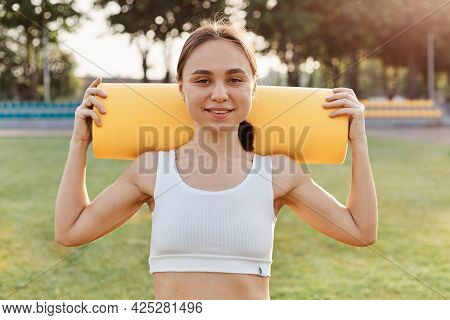 Good Looking Brunette Female Wearing White To Holding Yellow Karemat On Shoulders, Looking Smiling D