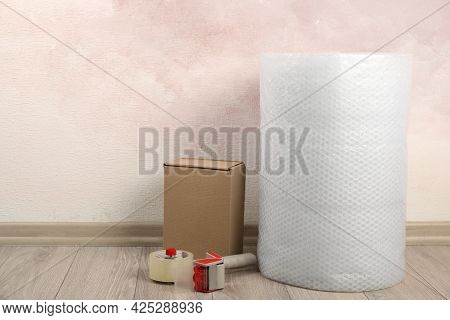 Bubble Wrap Roll, Tape Dispenser And Cardboard Box On Floor Near Pink Wall. Space For Text