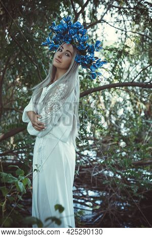 Beautiful Girl In Wreath Of Flowers In Forest. Portrait Of Young Beautiful Woman Wearing White Bride
