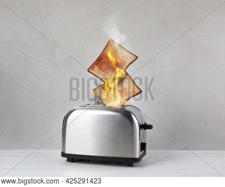 Toaster Flaming Up While Cooking Slices Of Bread On White Wooden Table. Unsafe Appliance