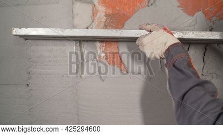 A Worker Plasters The Wall With A Spatula And Applies A Cement Mix Solution. The Repairman Lays The 