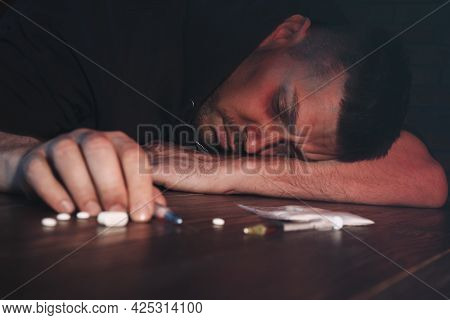 Overdosed Man Near Different Drugs At Table
