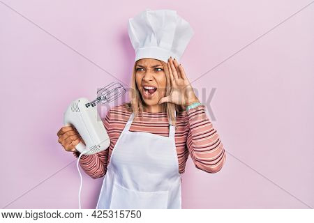 Beautiful hispanic woman holding pastry blender electric mixer shouting and screaming loud to side with hand on mouth. communication concept. 