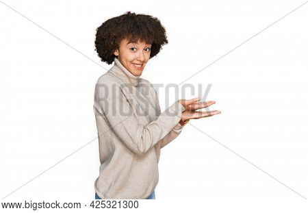Young hispanic girl wearing wool winter sweater pointing aside with hands open palms showing copy space, presenting advertisement smiling excited happy 