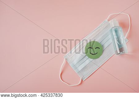 Green Healthy Smiling Face Paper Cut On Medical Face Mask And Bottle Of Blue Alcohol Gel On Sweet Pi