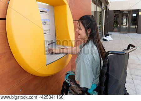 Happy Disabled Handicapped Woman In Wheelchair Using Atm Cash Macjine And Smiling At Camera On Sunny