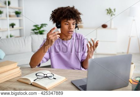 Home Based Education. Black Teen Guy In Headphones Communicating With Teacher Or Fellow Students On 