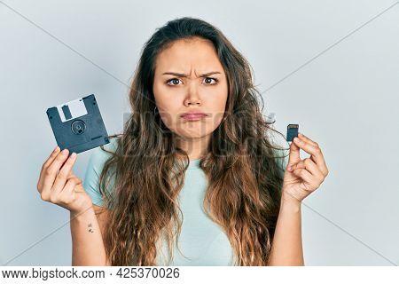 Young hispanic girl holding floppy disk and sdxc card skeptic and nervous, frowning upset because of problem. negative person. 
