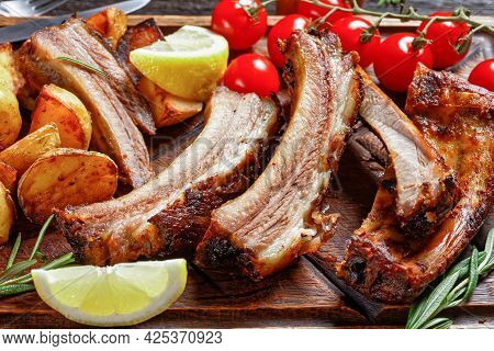 Grilled Pork Ribs Served With Roast New Potatoes And Fresh Tomatoes On A Wood Chopping Board On A Da