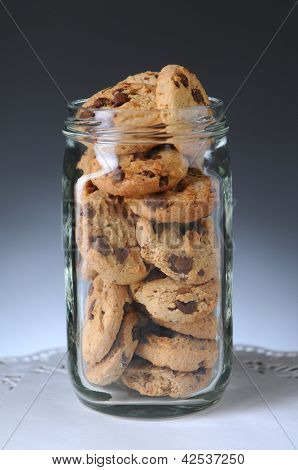 Nærbillede af et glaskrukke fuld af chokolade chip cookies. Lodret format på en lys til mørk grå Barbara