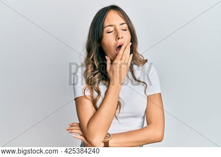 Young brunette woman wearing casual white t shirt bored yawning tired covering mouth with hand. restless and sleepiness. 