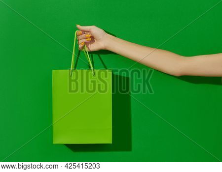 Womans Hand Holding Shopping Bag On Green Background. Shopping Sale Concept