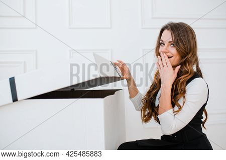 A Cute Girl Opens A Large Gift Box In Surprise Opening Her Mouth And Covering It With Her Hand