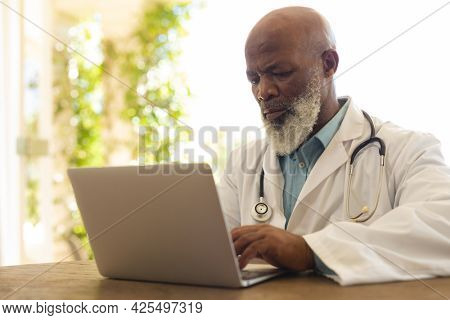 Portrait of senior african american male doctor in lab coat using laptop. medicine and healthcare services concept.