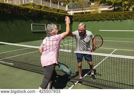 Senior caucasian couple playing tennis together on court highfiving. retirement retreat and active senior lifestyle concept.