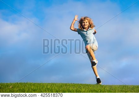 Little Adorable Boy Running On Grass. Excited Kid Play The Green Grass. The Child Has Blond Long Hai