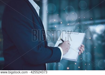 A Man In A Suit Holds An Empty File Folder(white Color)forward. And Sign The Document Blurred White 