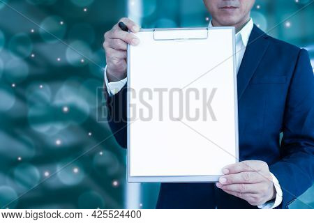 A Man In A Suit Holds An Empty File Folder(white Color)forward. Blurred White And Orange Lights Back