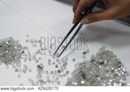 A Hand Holding Tweezers Transfers Diamonds From One Pile To Another. Discarding Precious Stones On A