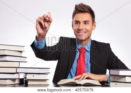 uomo d'affari giovane seduto alla sua scrivania piena di libri e scrivere qualcosa con il gesso su una imaginar