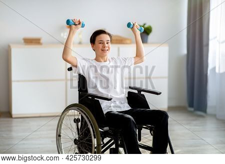 Physical Rehabilitation For Impaired People. Cheerful Disabled Teenager In Wheelchair Exerising With