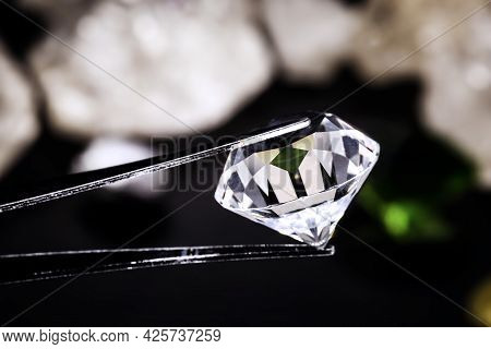 Cut Diamond Held By A Jeweler's Tweezers, With Rough Diamond Stones In The Background, Spot Focus