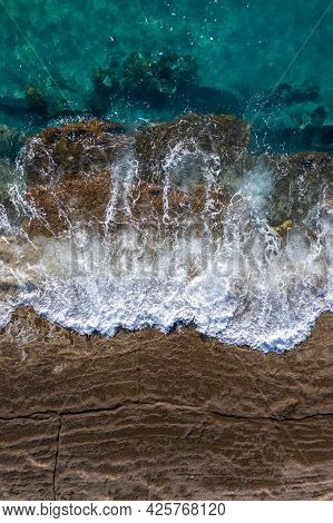 Waves Breaking On Brown Cliff Rocks With Rising Tide, Drone Perspective Directly Above