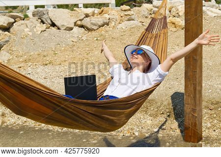 Work From Anywhere. Young Smilyng Woman, Female Freelancer In Straw Hat Working On Laptop On Beach.