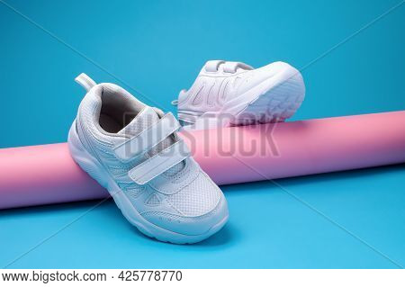 Promotional Picture Of A Balance Of Two White Girly Running Shoes On A Pink Long Paper Tube On A Blu