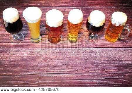 Six Glasses Of Different Types Of Beer Are In A Row On A Wooden Table.