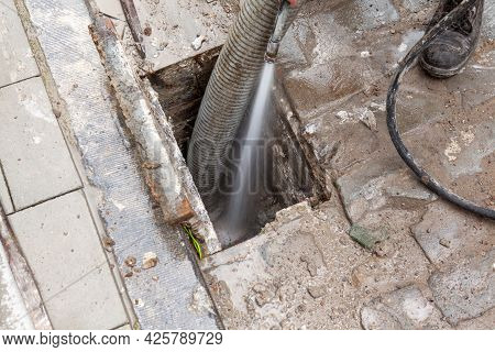 Next To A Foot Path There Is A Clogged Street Gully With Dirt And It Is Being Cleared By The Clearan