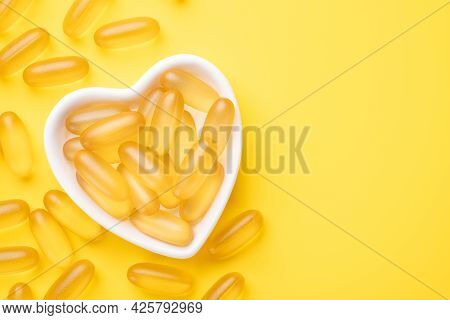 Vitamin D And Omega 3 Fish Oil Capsules Supplement In A Heart-shaped Plate On Yellow Background. Con
