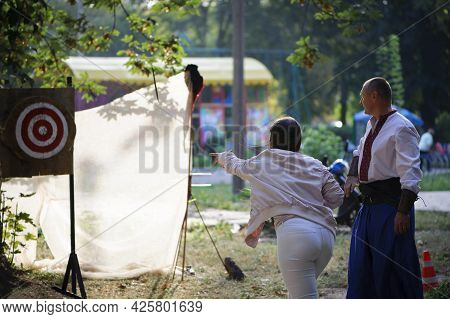 Girl Throws Knives At A Wooded Target. Woman With Red Hair Throwing Knife At Bullseye Target With A 