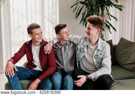 Three Male Friends Are Talking At The Green Sofa In Living Room. Guys Having A Talk, Sharing And Dis