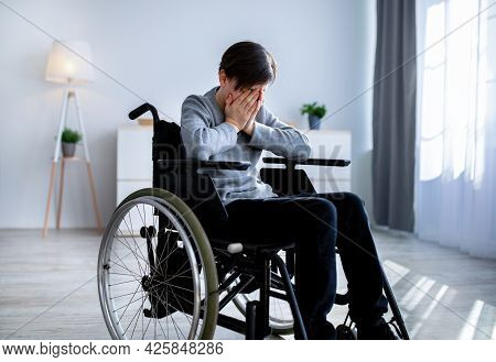 Depression In Disabled Teenagers. Unhappy Handicapped Teen Boy In Wheelchair Crying At Home