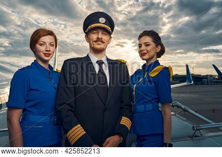 Smiling Pilot And Charming Stewardesses Standing On The Boarding Stairs