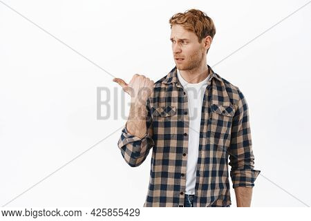 Skeptical Redhead Man Cringe From Something Bad, Looking And Pointing Left With Judging Disappointed