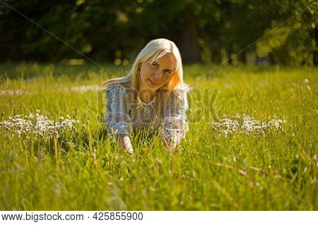 Peaceful Girl Lying On Green Grass With Stretched Arms And Legs. Blond Woman Lying On The Grass