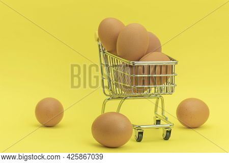 Raw Chicken Eggs In A Basket On A Yellow Background. Eggs In A Metal Cart On A Yellow Background. Ba