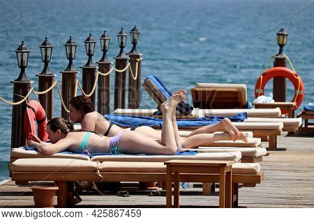 Hisaronu, Turkey - July 2021: Two Girls In Bikini Lying On Tanning Beds On A Beach. Tourists On Wood
