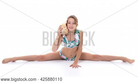 A Little Girl In A Swimsuit With A Shell. The Girl Offered A Shell To Her Ear, She Listens To The So