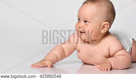 Portrait Six Month Old Baby Girl In A Diaper, Lying Down And Looking With Interest To The Side, Arms