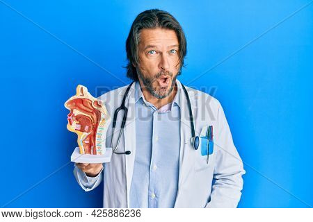 Middle age handsome otologist doctor man holding medical model scared and amazed with open mouth for surprise, disbelief face 